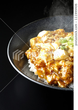 一張黑色背景下滾燙的麻婆碗的照片,上面放著大量的豆腐和蔥 一張黑色背景下滾燙的麻婆碗的照片,上面放著大量的豆腐和蔥 111999406