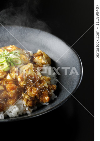 一張黑色背景下滾燙的麻婆碗的照片，上面放著大量的豆腐和蔥 111999407