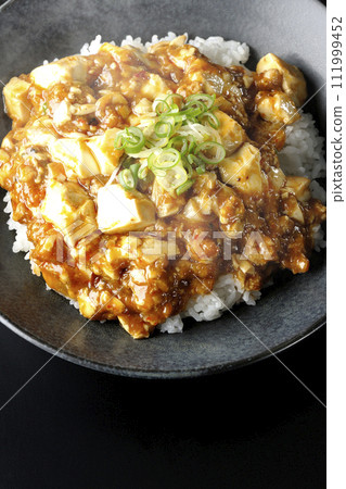 黑色背景下滾燙的麻婆碗的頭頂照片，上面放著大量的豆腐和蔥 111999452