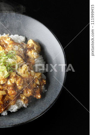 黑色背景下滾燙的麻婆碗的頭頂照片，上面放著大量的豆腐和蔥 111999455