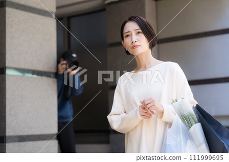 A person hiding in a building and taking a photo of a woman A person hiding in a building and taking a photo of a woman 111999695
