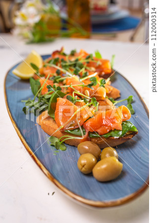 salmon with lemon, olives and microgreens on a blue plate on the table 112000314