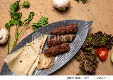 Top view of delicious kebabs lula lamb kebab with grilled vegetables and herbs on a wooden table. 112000428