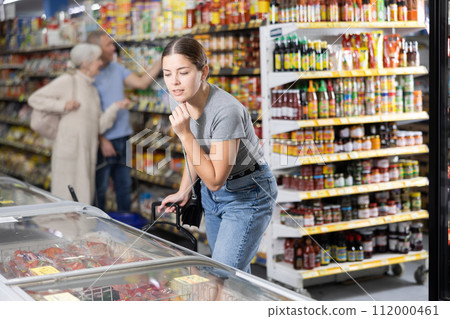 Young woman looking at products in glass refrigerator in store 112000461
