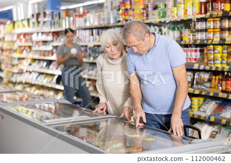 Man and woman purchasers choosing frozen product in supermarket Man and woman purchasers choosing frozen product in supermarket 112000462