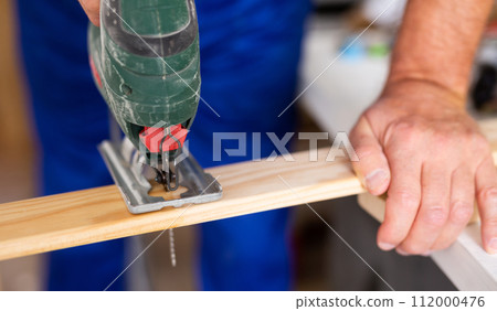 Work with an electric jigsaw - cutting wooden board close-up Work with an electric jigsaw - cutting wooden board close-up 112000476