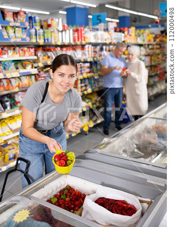 Young woman shopping for frozen strawberries in the grocery section of supermarket Young woman shopping for frozen strawberries in the grocery section of supermarket 112000498