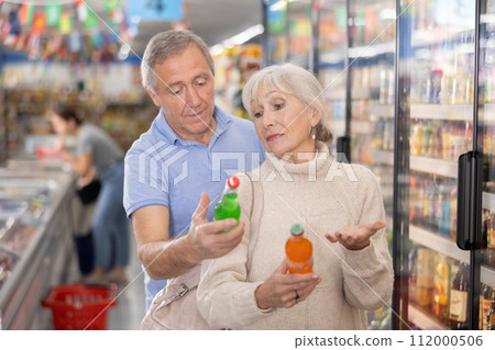 Elderly couple choosing sweet sodas together in the grocery section of supermarket 112000506