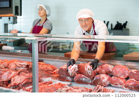 Elderly male seller shows demonstrates raw beef ribs in glass showcase of refrigerator Elderly male seller shows demonstrates raw beef ribs in glass showcase of refrigerator 112000525