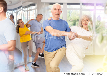 Group of mature men and woman in sportswear learning to dance latin salsa dance in dance class 112000529