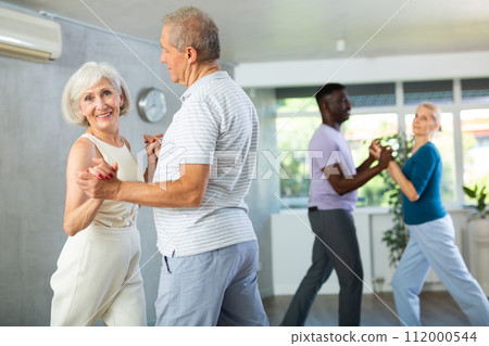 Mature men and women practicing Ballroom dances in training room Mature men and women practicing Ballroom dances in training room 112000544