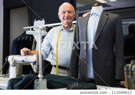 Experienced tailor threading jacket before starting work in workshop 112000622