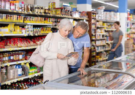 Man and woman purchasers choosing frozen product in supermarket 112000633