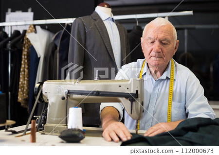 Portrait of elderly tailor working on sewing machine at studio Portrait of elderly tailor working on sewing machine at studio 112000673