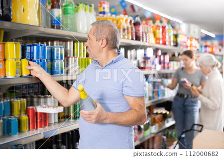 Aged man reading labels while choosing soft drink in supermarket 112000682