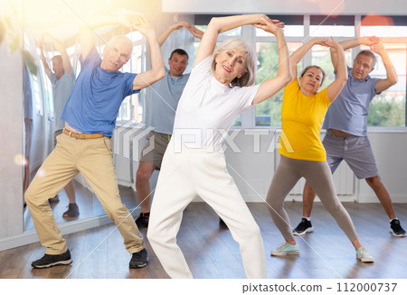 Elderly woman practicing Tai Chi with group in training room 112000737