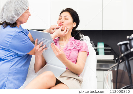 Cosmetologist consulting female patient in medical esthetic office 112000830