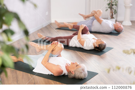 Group of elderly people doing yoga on mat in studio Group of elderly people doing yoga on mat in studio 112000876