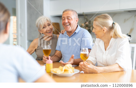 Cheerful elderly women and man gathering around kitchen table 112000896
