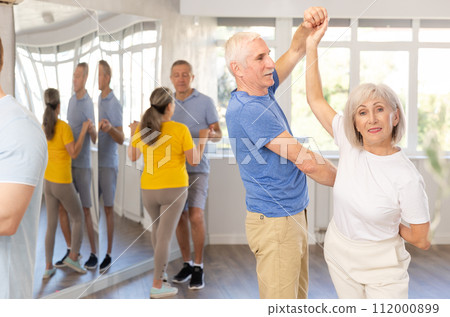 Senior woman practicing passionate samba with man in dance class Senior woman practicing passionate samba with man in dance class 112000899