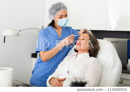 Cosmetologist giving beauty injections to elderly female client 112000958