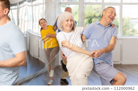 Enthusiastic senior couple practicing jive in group dance class Enthusiastic senior couple practicing jive in group dance class 112000962