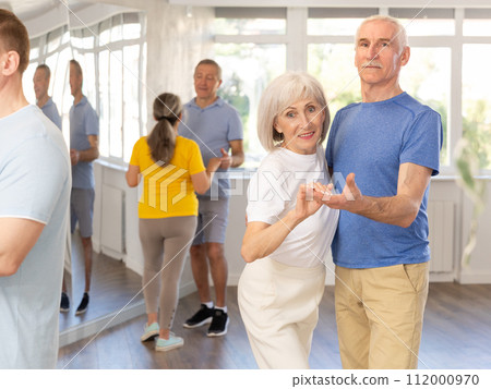 Elderly man in dance hall with female partner and dances Latin rumba. Hobby, healthy lifestyle concept Elderly man in dance hall with female partner and dances Latin rumba. Hobby, healthy lifestyle concept 112000970