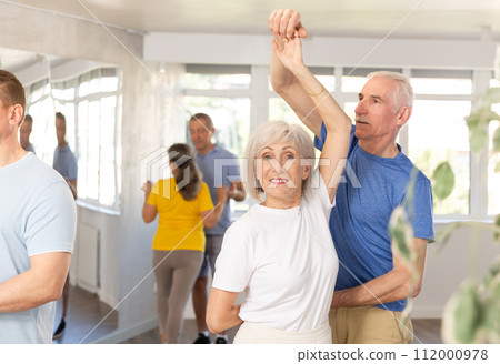 Senior man dancing bachata with female partner during group class 112000978