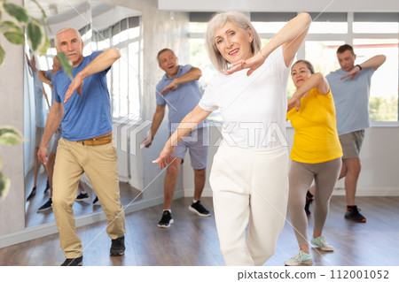 Elderly woman practicing Tai Chi with group in training room 112001052