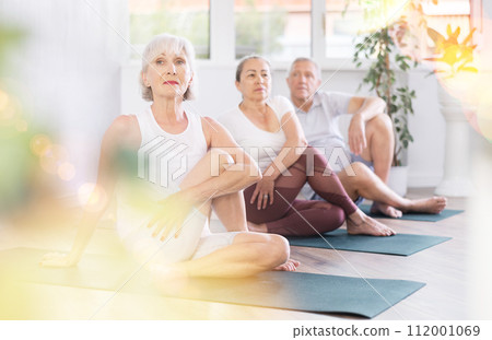 Group of elderly people doing yoga on mat in studio Group of elderly people doing yoga on mat in studio 112001069