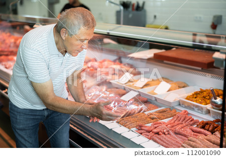 Elderly man buyer of meat department of store, looking at meat small sausage in refrigerator window Elderly man buyer of meat department of store, looking at meat small sausage in refrigerator window 112001090
