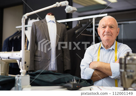 Portrait of an accomplished positive tailor with crossed arms in workshop 112001149