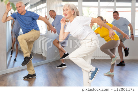 Cheerful elderly woman learning dynamic dances at group choreography lesson 112001172