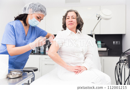 Professional nurse giving antiviral injection to aged woman Professional nurse giving antiviral injection to aged woman 112001215