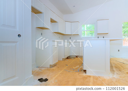 In newly constructed house, wooden white kitchen cabinets are being installed In newly constructed house, wooden white kitchen cabinets are being installed 112001526