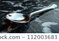 A classic silver spoon lies on a dark marbled surface with reflections. 112003683