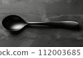 A matte black spoon on a textured grey concrete surface with subtle highlights. 112003685