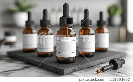 Multiple amber dropper bottles with blank white labels on a black slate coaster, in a modern kitchen setting. 112003697