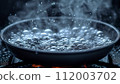 A close-up of a skillet on the stove with water boiling vigorously, showcasing the bubbles and steam in a kitchen setting. 112003702
