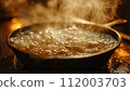 Steaming hot water boils in a pan, with a golden glow reflecting off the bubbles, creating a warm kitchen atmosphere. 112003703