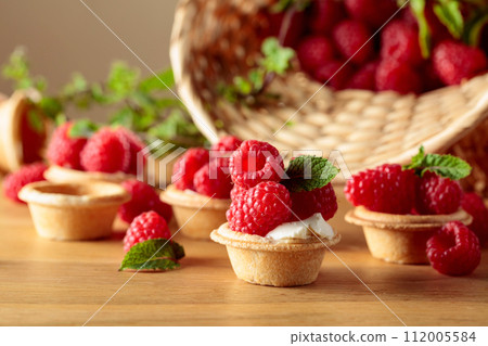 Tartlets with fresh raspberries and mint on a wooden table. Tartlets with fresh raspberries and mint on a wooden table. 112005584