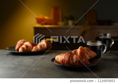 Fresh baked croissants and black coffee on a kitchen table. Fresh baked croissants and black coffee on a kitchen table. 112005601