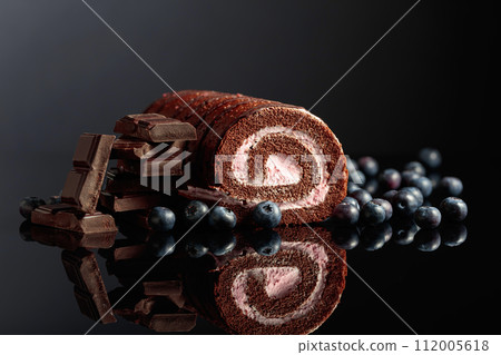 Chocolate roll cake with blueberries and a broken black chocolate bar. Chocolate roll cake with blueberries and a broken black chocolate bar. 112005618