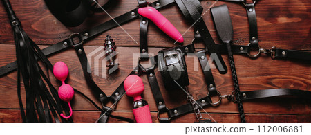 set of BDSM sex toys with handcuffs, whip flogger and vibrator for submission and female masturbation and orgasm on a wooden background set of BDSM sex toys with handcuffs, whip flogger and vibrator for submission and female masturbation and orgasm on a wooden background 112006881