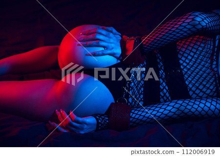 submissive woman with a sexy body and big ass with hands in BDSM handcuffs lies on bed in bedroom. Slave girl for sex with submission and domination 112006919