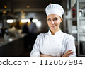 Professional female chef. A young woman standing proudly in professional kitchen. Culinary Artistry, chef's passion for gastronomy and dedication, culinary innovation 112007984