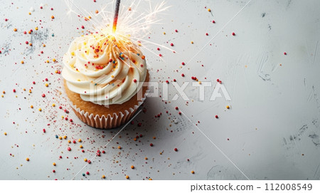 An overhead shot of a single cupcake with a sparkler, against a stark white background 112008549