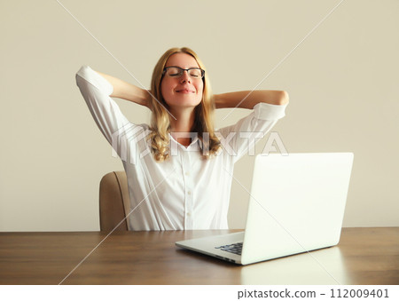Relaxed happy woman take a break working with laptop sitting at desk in office or home 112009401