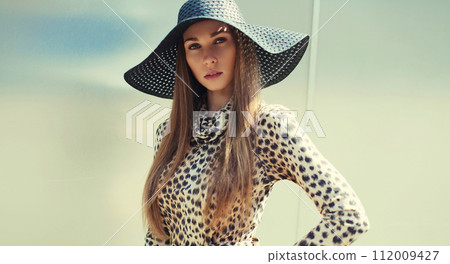 Portrait of beautiful blonde young woman wearing summer straw hat, leopard dress Portrait of beautiful blonde young woman wearing summer straw hat, leopard dress 112009427
