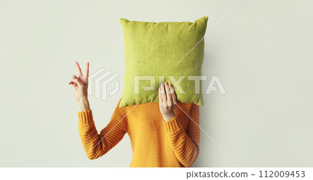 Healthy sleep, woman holding colorful soft pillow covering her head at home in morning 112009453
